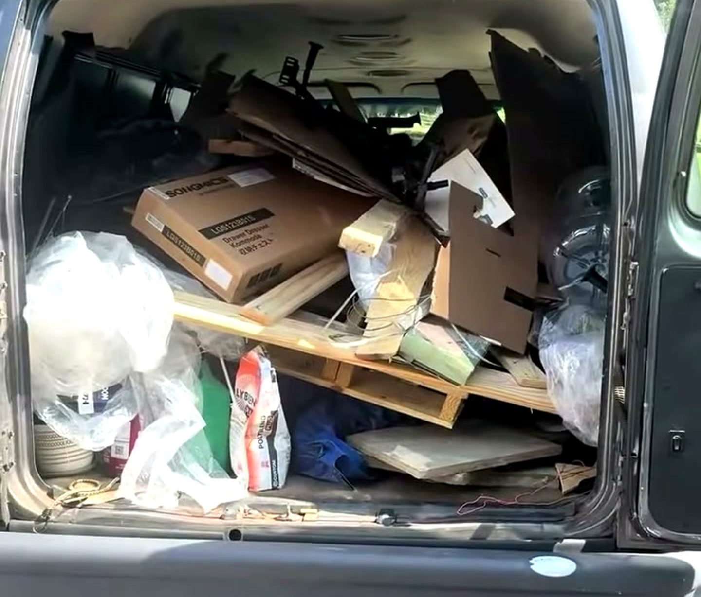 A garage part way through a cleanout, a ride-on mower and stacked household junk in the foreground and the Bin Movers van backed up to the open door.