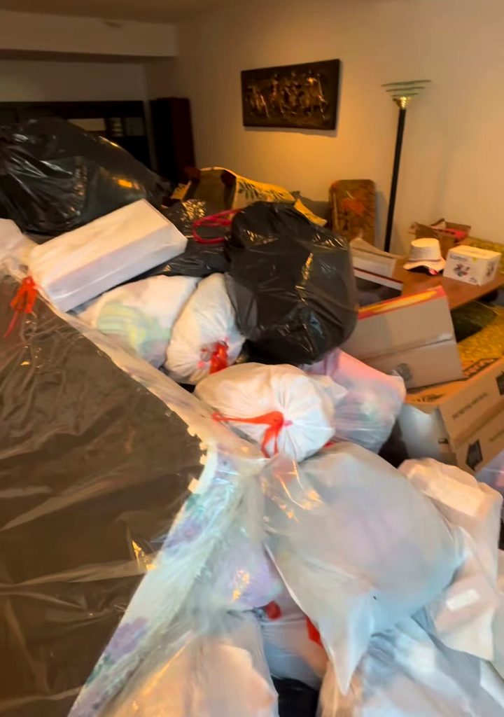 A living room packed to the ceiling with bagged household junk and stacked furniture, before a cleanout.
