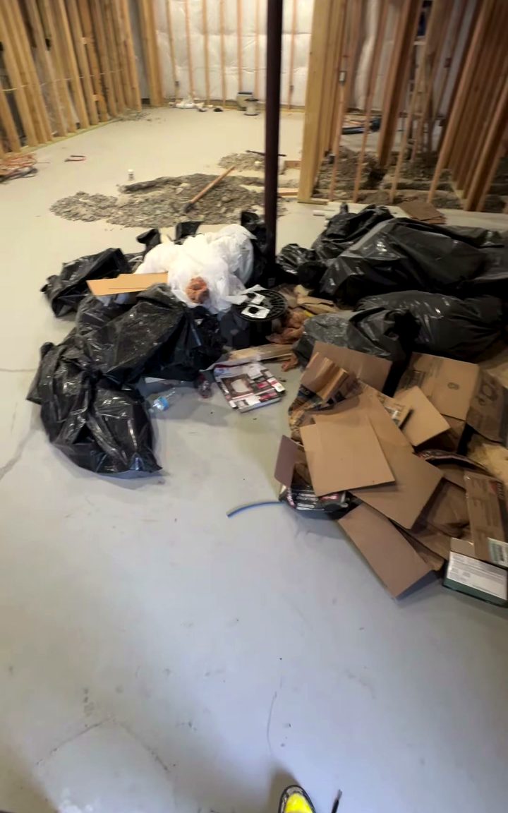 Black rubbish bags and flattened cardboard piled on the bare concrete floor of a part-built room.